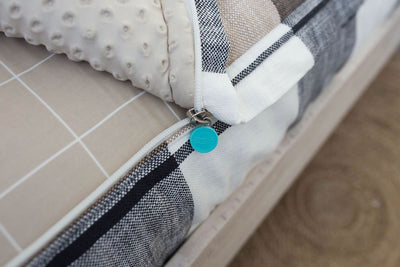 A close up view of a bed made with charcoal, cream and tan plaid zipper bedding with the bed slightly unzipped to reveal the minky comforter and the tan and white grid pattern bottom cotton lining.