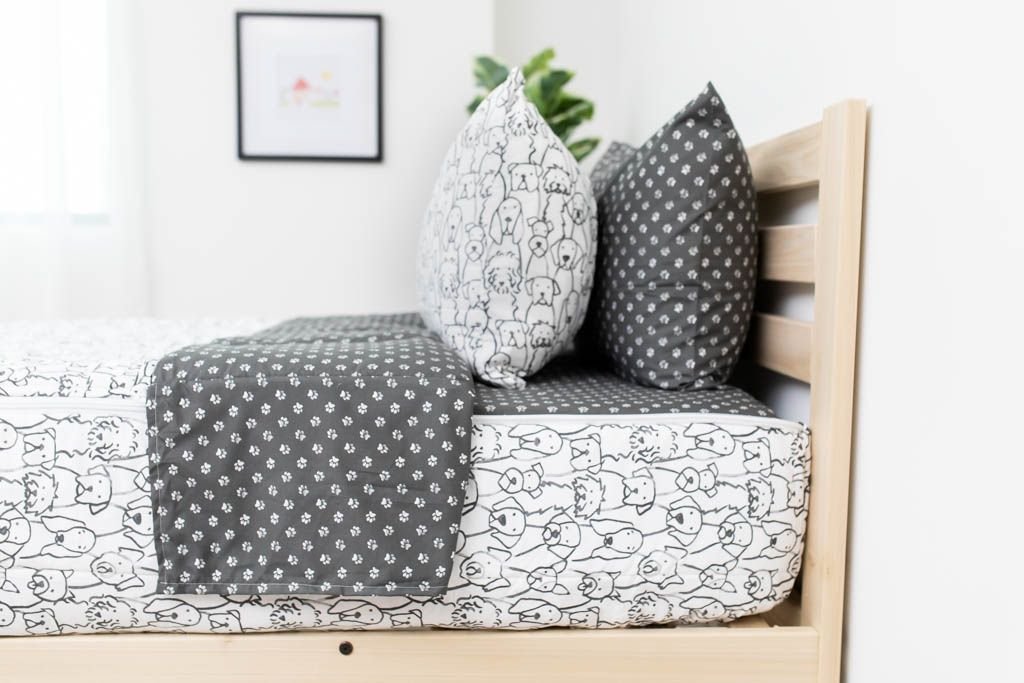 A side shot of a twin bed made with charcoal and white pattern dogs zipper bedding, the top unzipped and pulled back slightly and two pillows at the head of the bed.