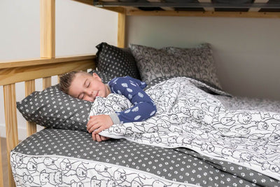 A young boy in blue pajamas sleeping in a bed made with charcoal and white pattern dogs kids zipper bedding.