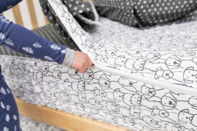 A young boy in blue pajamas pulling the zipper closed on a set of charcoal and white pattern dogs kids zipper bedding