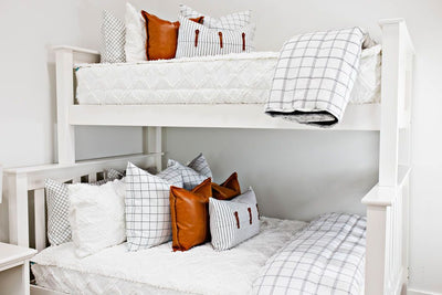 Bunk bed with White queen bedframe with white and black grid pattered bedding, faux leather pillows, white and black striped lumbar with faux lather buckles and white and black grid pattered blanket