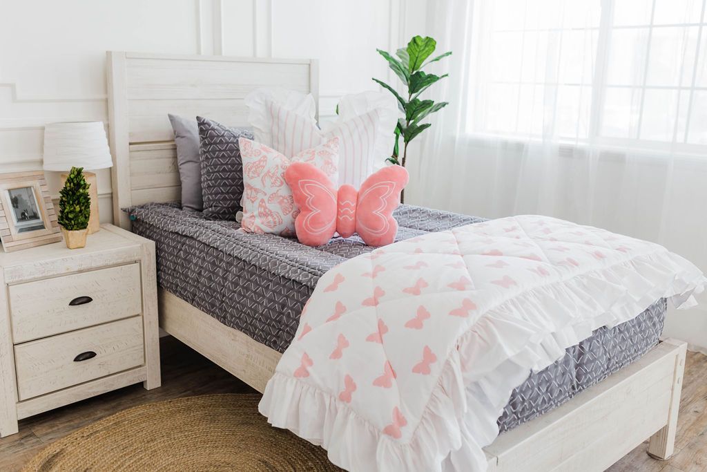 twin bed with Gray bedding with textured diamond and white striped euro with ruffle, white and pink butterfly print pillow, pink plush butterfly pillow, and white and pink print blanket with white ruffle along the edge