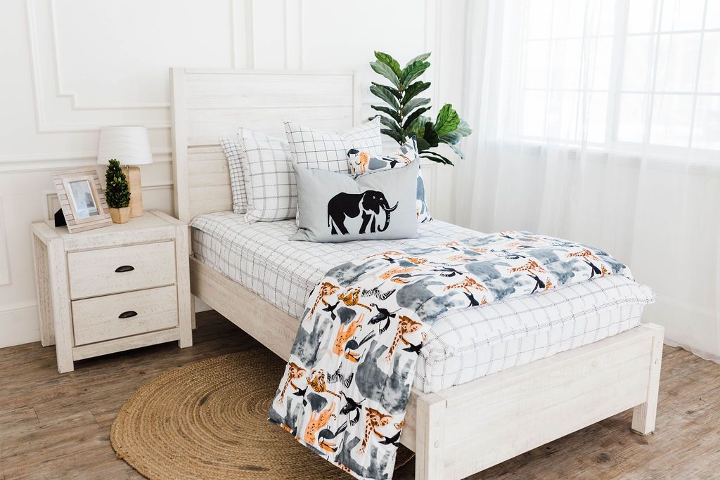 White twin bedframe with white and black grid patterned bedding, white and black grid euro, safari animal print pillow, gray lumbar with embroidered elephant, and safari animal print blanket