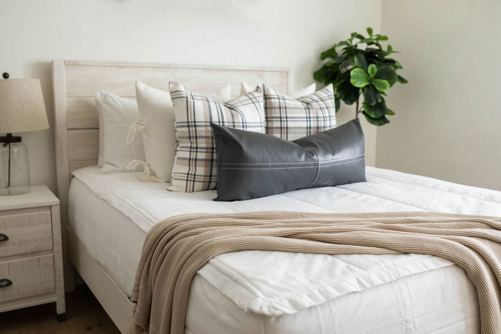 A bed made with white woven plaid zipper bedding and an assortment of neutral throw pillows and blanket.