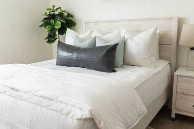 A queen bed made with white woven plaid zipper bedding and an assortment of striped and neutral pillows and a matching blanket at the end of the bed.