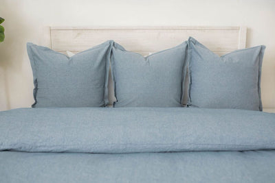 A bed made with a blue two-toned zipper duvet folded and matching large pillows. 
