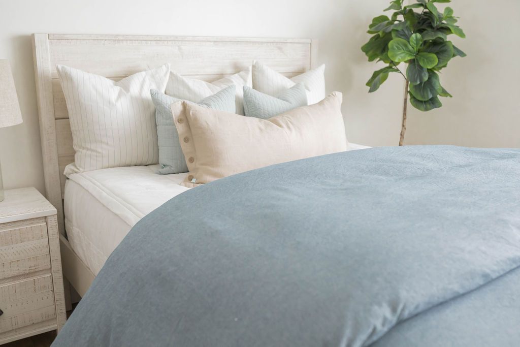 A brightly lit bedroom with a bed made with white zipper bedding and a blue two-tone zipper duvet folded half way down the bed and adorned with neutral pillows.