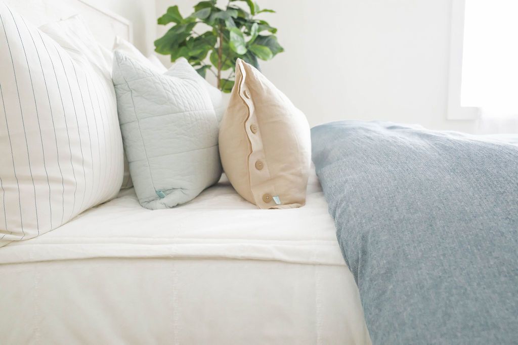 A side view of a bed made with white zipper bedding and a blue two-toned zipper duvet folded half way down the bed and adorned with neutral and light blue pillows.