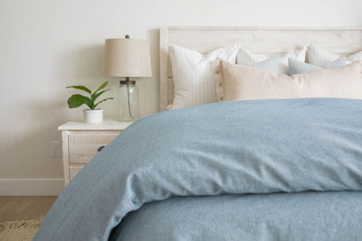 A bed made with a blue two-toned zipper duvet folded half way down the bed and adorned with neutral pillows.