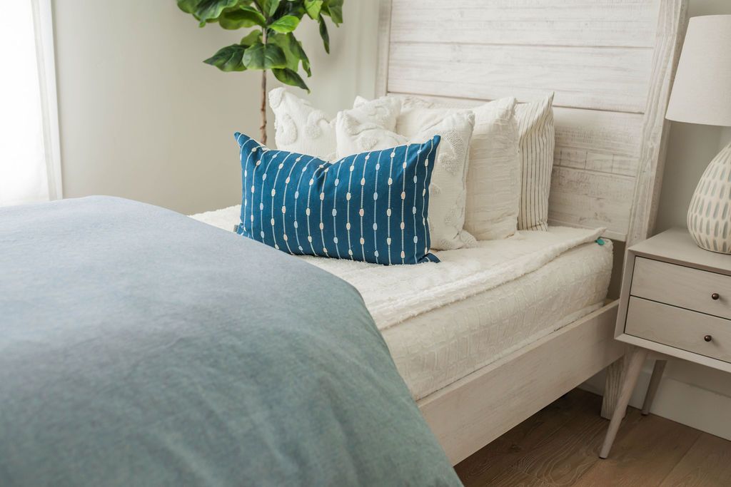 A brightly lit bedroom with a bed made with cream textured zipper bedding and a blue two-tone zipper duvet folded half way down the bed and adorned with neutral and blue pillows.