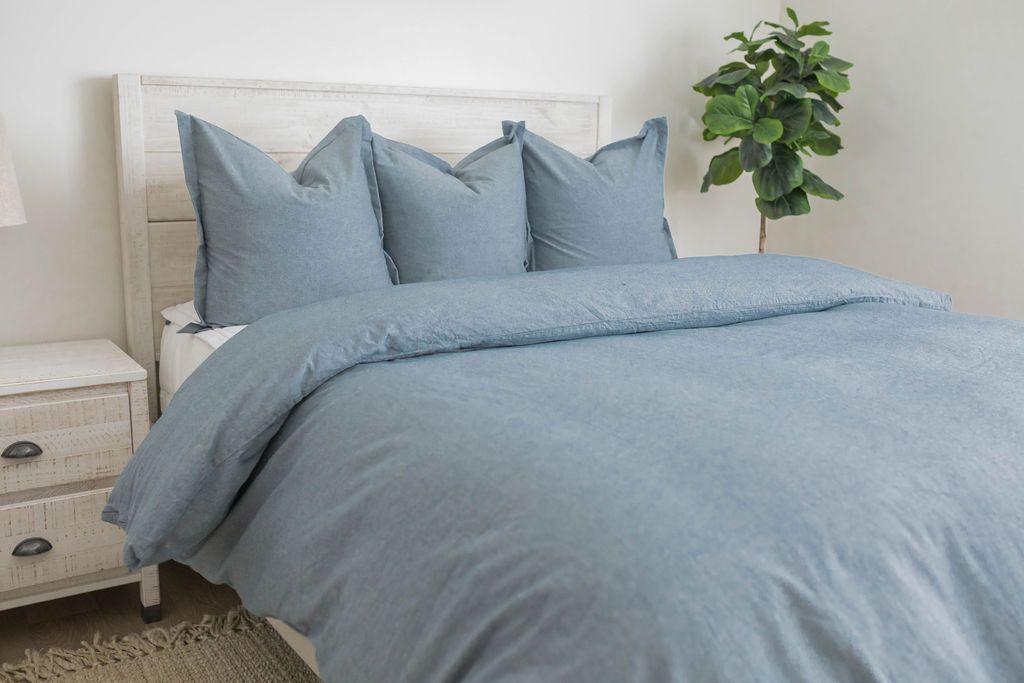 A queen bed made with white zipper bedding and a blue duvet cover over it and matching blue large pillows at the top of the bed.