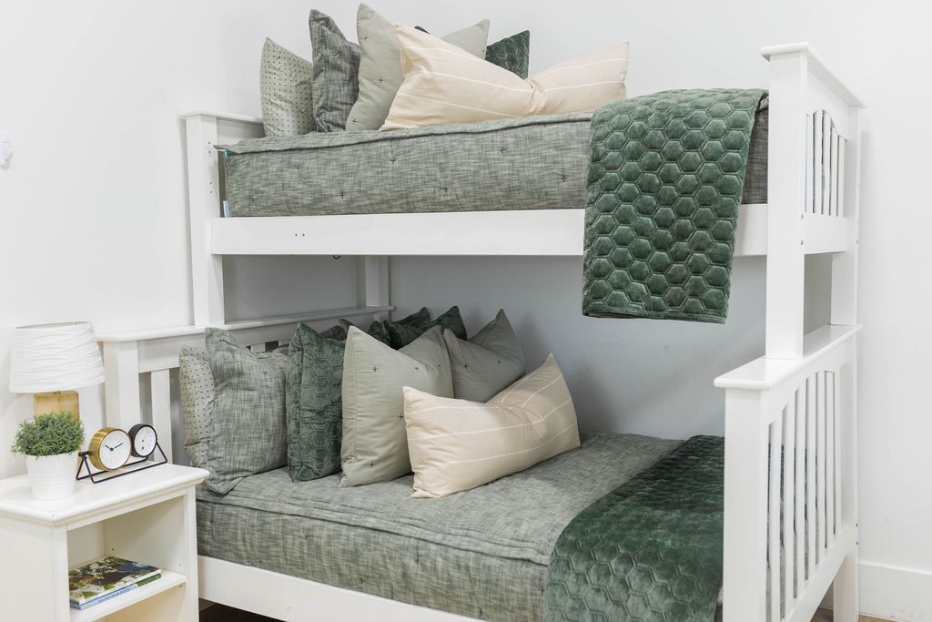 A standard bunk bed with both bunks made with deep emerald green zipper bedding and neutral and green velvet pillows and blankets.