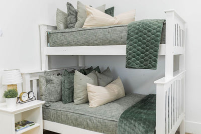 A standard bunk bed with both bunks made with deep emerald green zipper bedding and neutral and green velvet pillows and blankets.