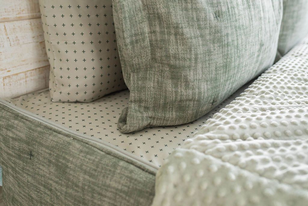A bed made with dark and khaki green zipper bedding with the comforter pulled back and pillows on top of the bed.