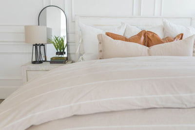 A bed made with a tan and white striped zipper duvet folded half way down the bed and adorned with neutral pillows.