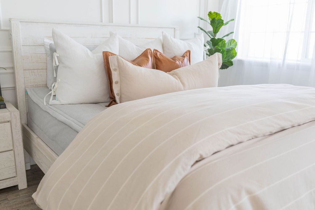 A brightly lit bedroom with a bed made with light gray waffle textured zipper bedding and a tan and white striped zipper duvet folded half way down the bed and adorned with neutral pillows.