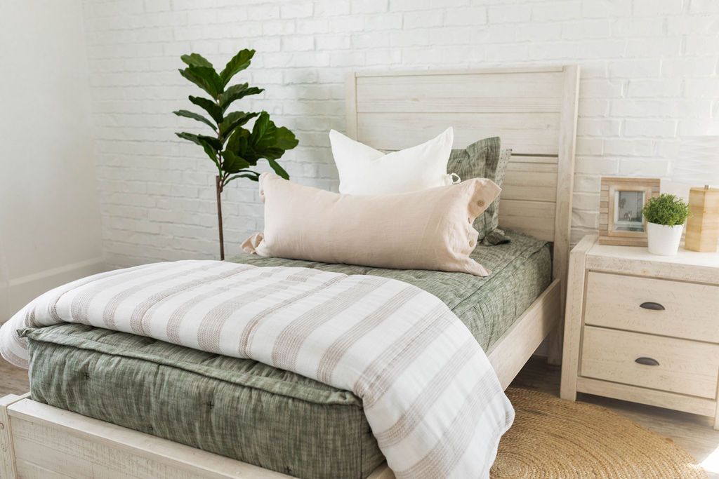 A twin bed made with deep emerald green zipper bedding and white and tan pillows and blanket.