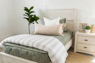A twin bed made with deep emerald green zipper bedding and white and tan pillows and blanket.