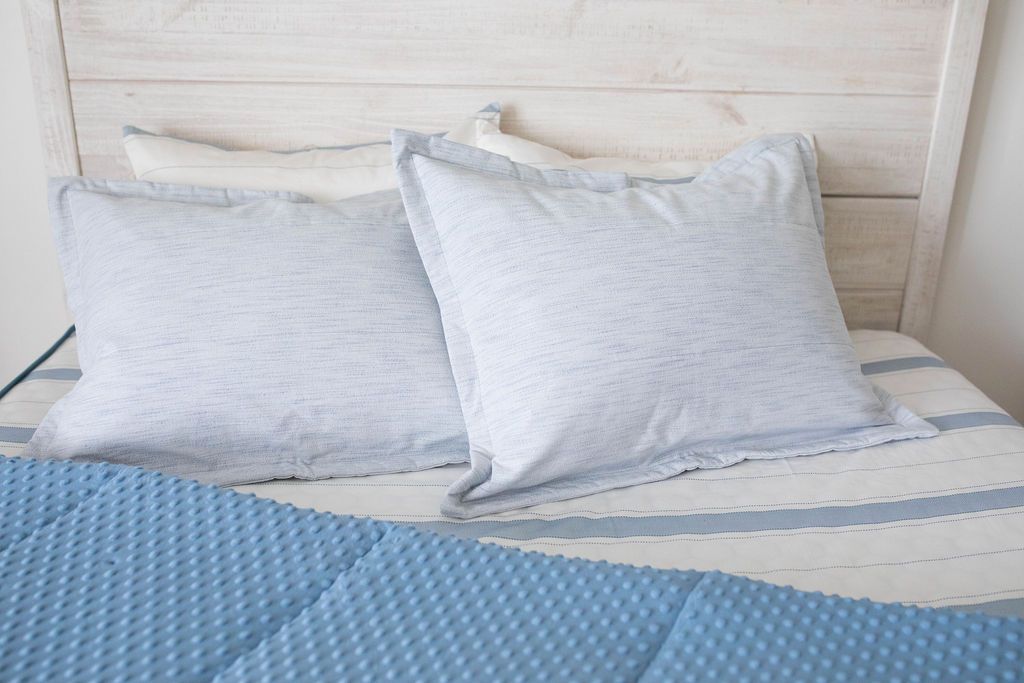 A bed made with light blue zipper bedding with the comforter pulled back revealing a striped interior and pillows on top of the bed.