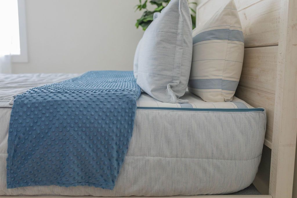 A side view of a bed made with light blue zipper bedding with the top unzipped halfway down the bed and the minky interior comforter folded down.