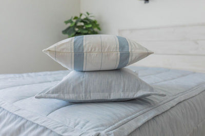A light blue zipper bedding made with matching pillows stacked in the middle of the bed. 