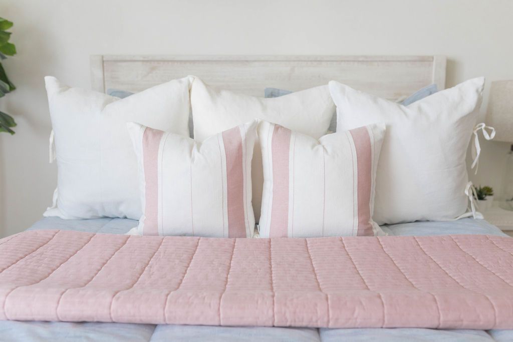 A close up of a bed made with light blue zipper bedding with neutral pillows and coordinating folded pink blanket.