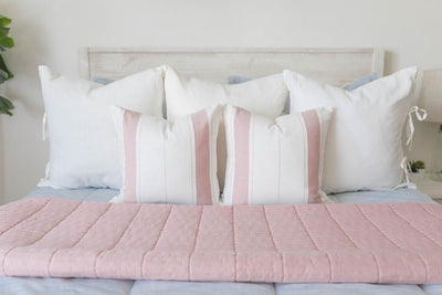 A close up of a bed made with light blue zipper bedding with neutral pillows and coordinating folded pink blanket.