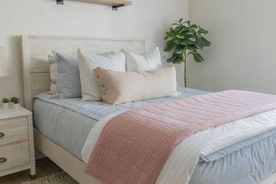 A queen bed made with light blue zipper bedding and neutral striped pillows and matching blankets. 