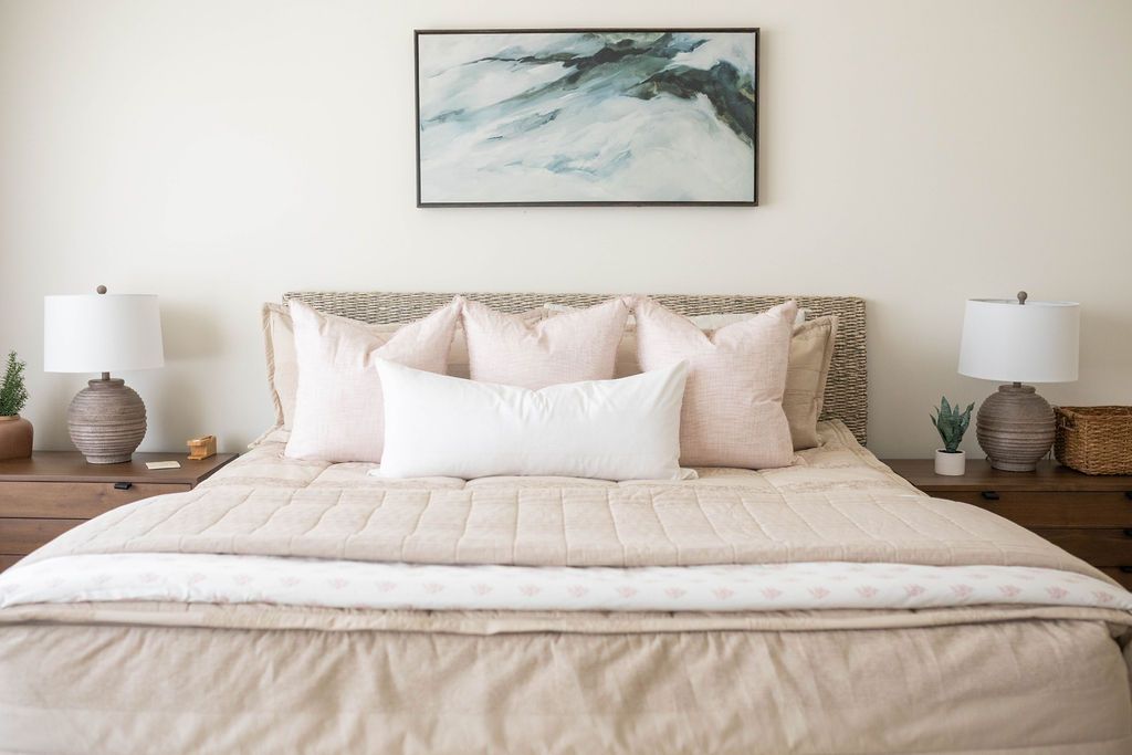 A bed made with tan zipper bedding and an assortment of neutral and light pink throw pillows and matching blankets at the end of the bed.