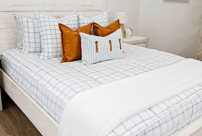 White queen bedframe with white and black grid pattered bedding, faux leather pillows, white and black striped lumbar with faux lather buckles and white and black grid pattered blanket