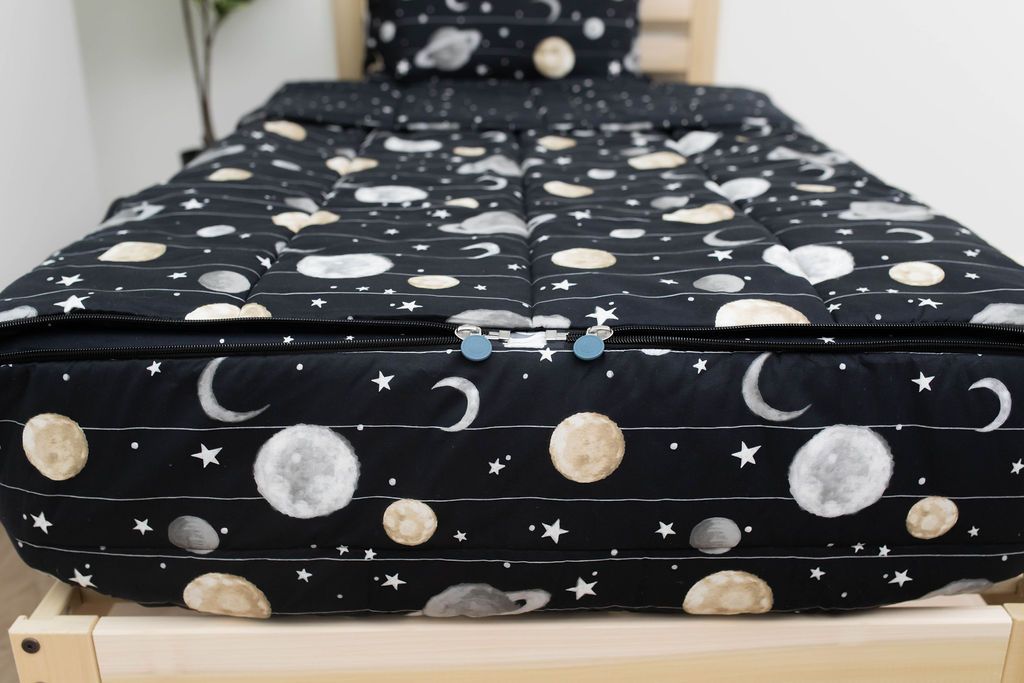 The foot of a bed made with black planets and stars kids zipper bedding showing where the two zippers are located.