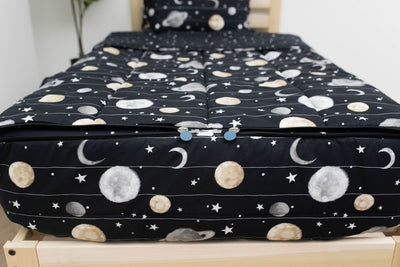 The foot of a bed made with black planets and stars kids zipper bedding showing where the two zippers are located.