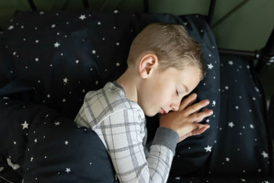 A young boy in gray pattern pajamas sleeping in a bed made with black planets and stars kids zipper bedding.