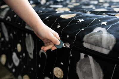A young boy pulling the zipper closed on a set of black planets and stars kids zipper bedding.