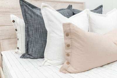 A close up view of a bed made with white and black striped zipper bedding and an assortment of neutral pillows.
