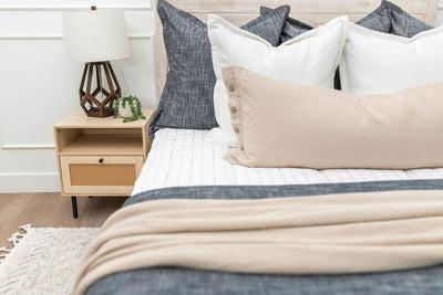 A close up view of a bed made with white and black striped zipper bedding and an assortment of neutral and charcoal gray pillows and blankets.