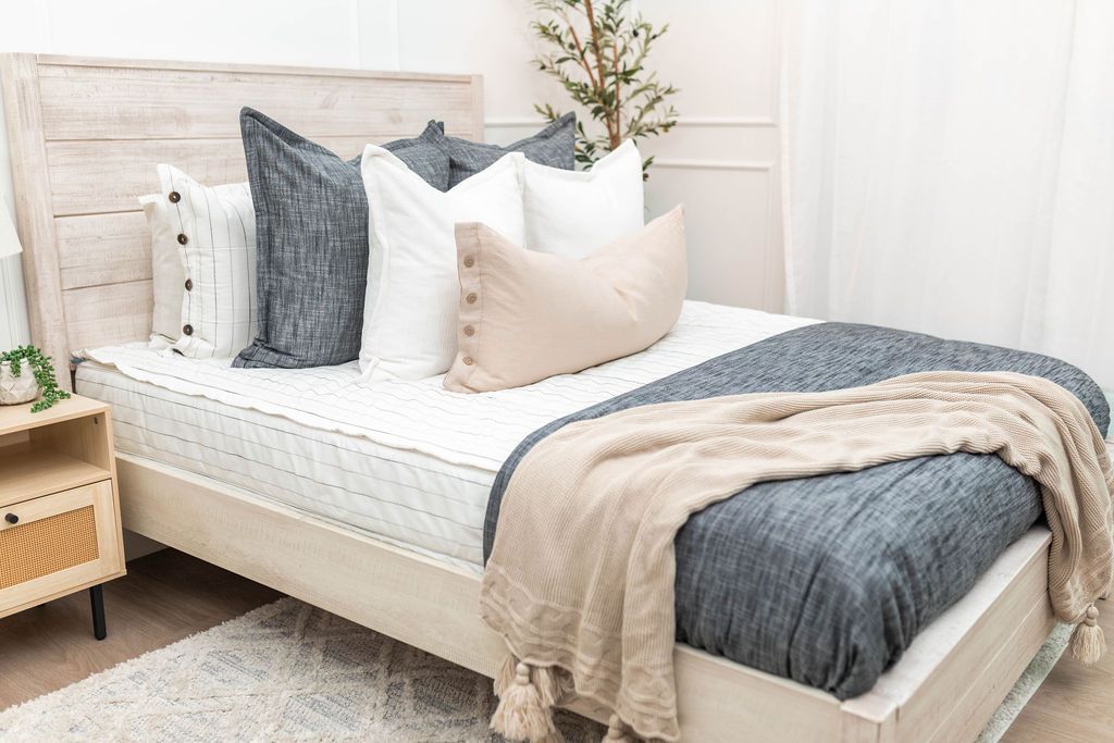A bed made with white and pinstripes zipper bedding and an assortment of neutral and dark gray pillows and blankets.