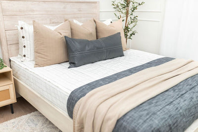 A bed made with white and pinstripes zipper bedding and an assortment of neutral pattern and dark gray pillows and blankets.