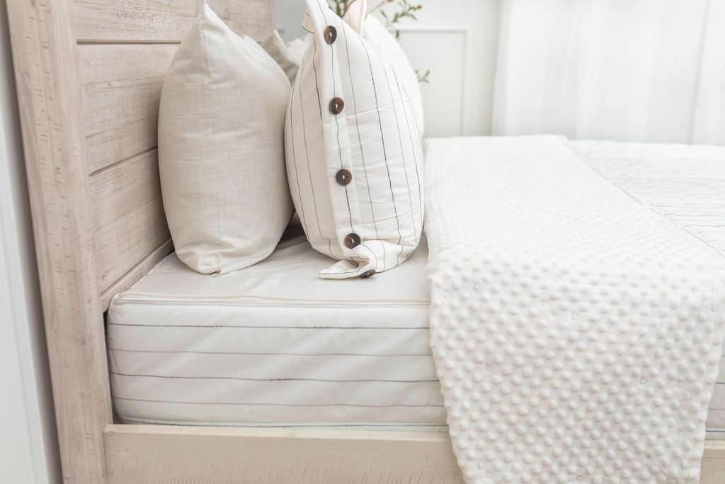 A close up side view of a bed made with white and pinstripes zipper bedding with the top unzipped halfway down the bed and the comforter folded down.