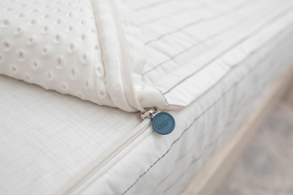 A close up view of a bed made with white and pinstripes zipper bedding with the bed slightly unzipped to reveal the minky comforter and white pattern bottom cotton lining.