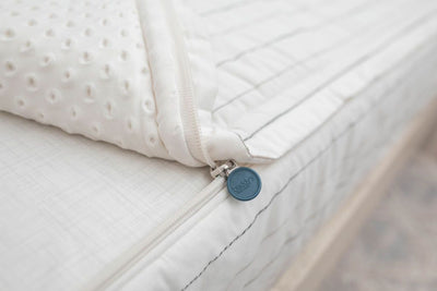 A close up view of a bed made with white and pinstripes zipper bedding with the bed slightly unzipped to reveal the minky comforter and white pattern bottom cotton lining.
