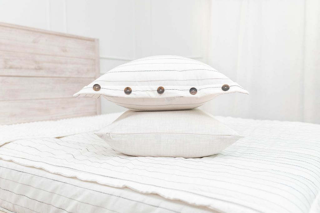 A bed made with white and pinstripes zipper bedding and matching pillows stacked on top of each other in the middle of the bed.