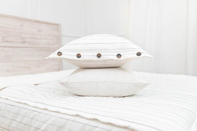 A bed made with white and pinstripes zipper bedding and matching pillows stacked on top of each other in the middle of the bed.