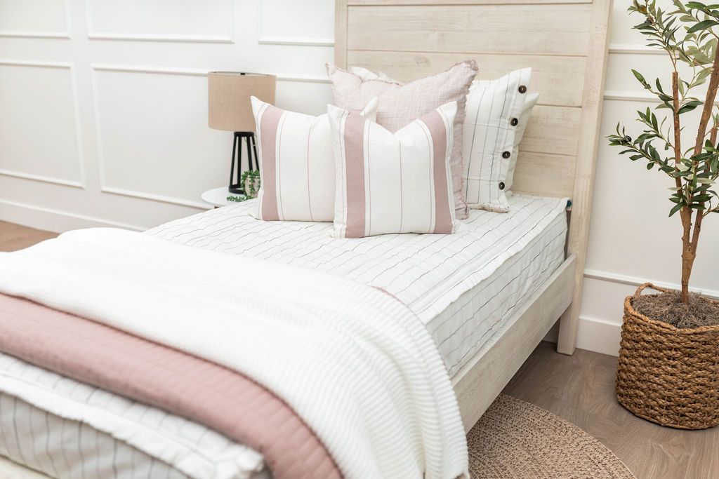 A twin bed made with white and pinstripes zipper bedding and light pink and white striped pillows and blankets.