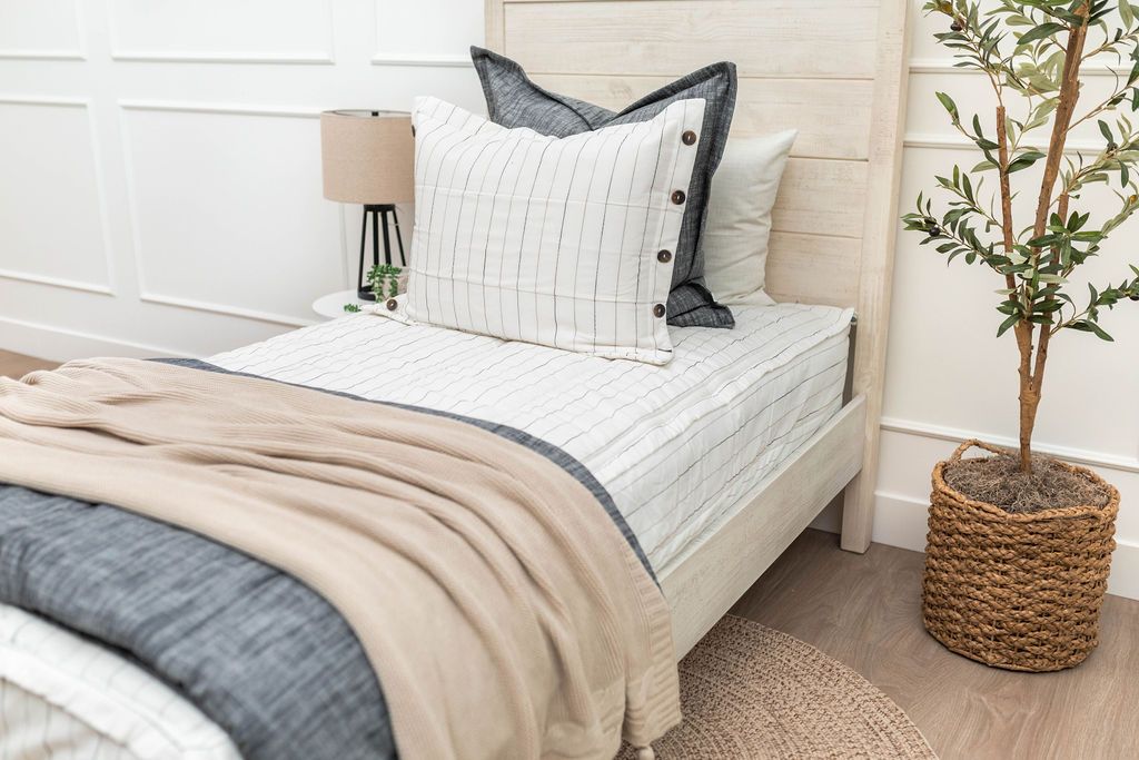 A twin bed made with white and pinstripes zipper bedding and dark gray charcoal and striped pillows and blankets.