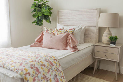 A twin bed made with white woven plaid zipper bedding and an assortment of pink and multi-color floral pattern pillows and blanket.