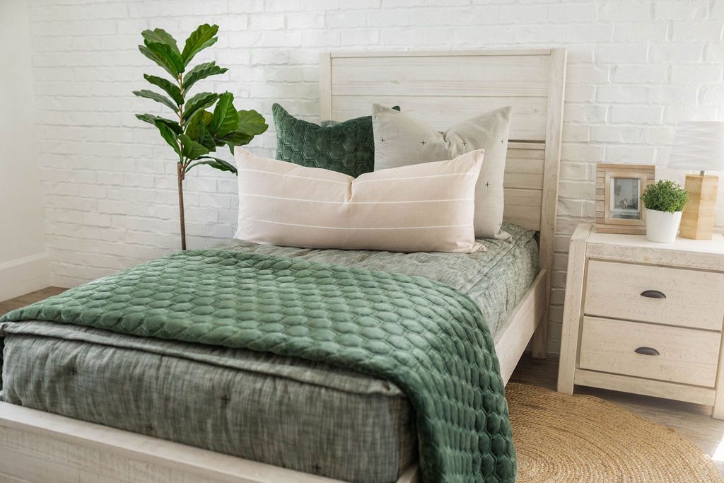 A twin bed made with emerald green zipper bedding and an assortment of neutral green pillows and matching velvet blanket. 
