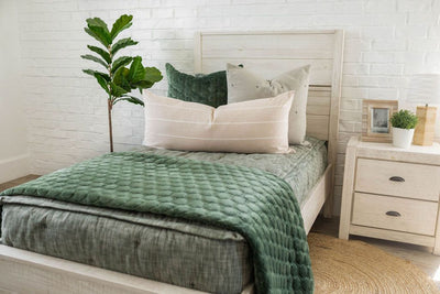 A twin bed made with emerald green zipper bedding and an assortment of neutral green pillows and matching velvet blanket. 