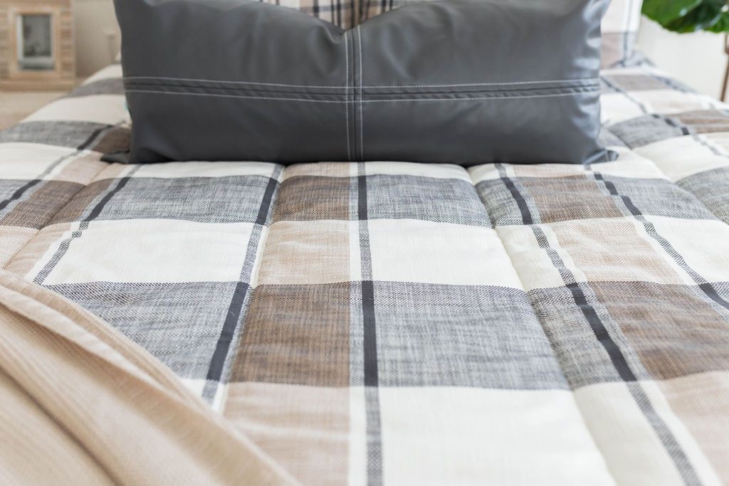 Gray, cream and white plaid zipper bedding with black leather lumbar pillow and brown throw blanket. 