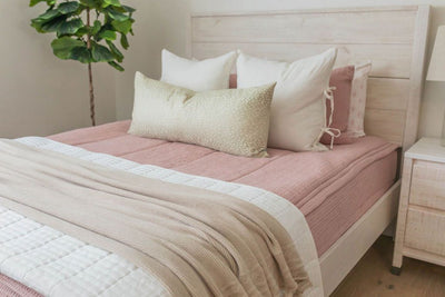 Pink zipper bedding with white and pink pillows and shams. White and cream throw blankets and cream lumbar pillow